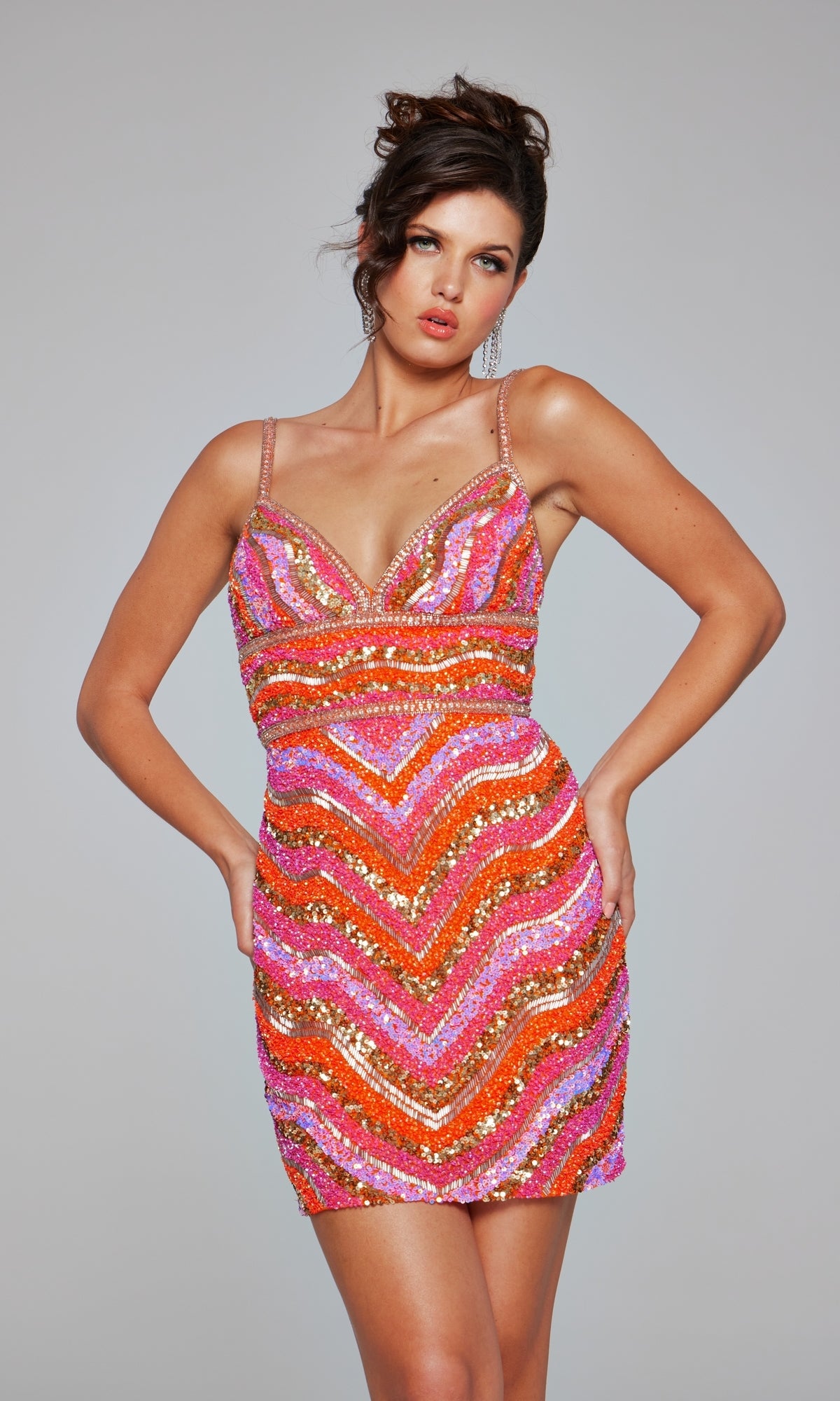 A woman wears the Beaded Short Striped Hoco Dress: Jovani 39903— a sleeveless, V-neck orange and pink sequin mini with gold chevron stripes—standing against a plain gray background.